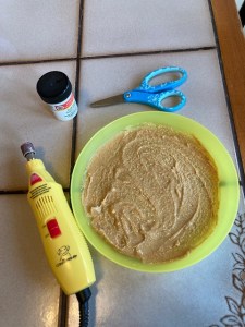 a yellow nail grinder, a plastic plate smeared with peanut butter, blunt scissors and styptic powder are gathered for the pedicure