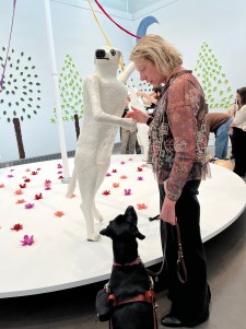 Deni and black Lab Hildy look closely at a 5-foot, white sculpture of a playful dog, London, who is standing on her hind legs.